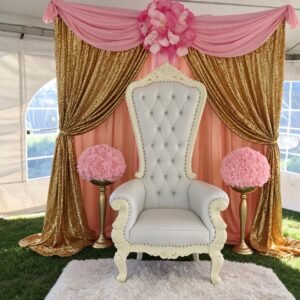 Pink and gold throne chair backdrop package featuring a white tufted throne chair, gold sequin curtains, pink draping and floral arrangements