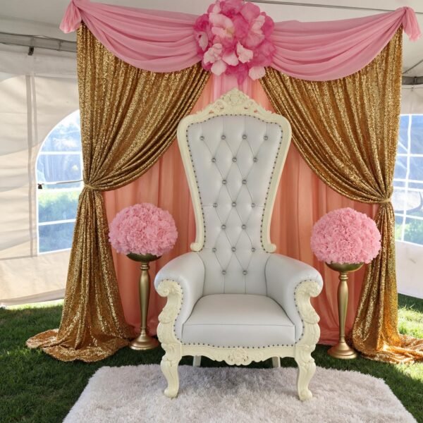 Pink and gold throne chair backdrop package featuring a white tufted throne chair, gold sequin curtains, pink draping and floral arrangements